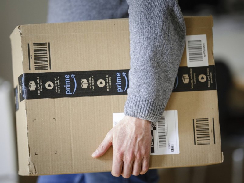 Mann trägt ein Amazon-Paket unter dem Arm