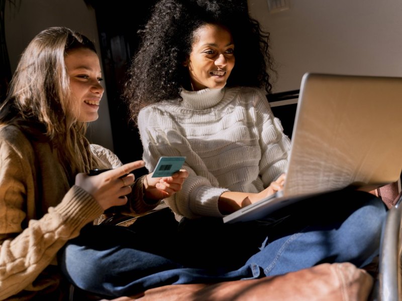 Zwei Frauen sitzen mit Laptop und Kreditkarte da.