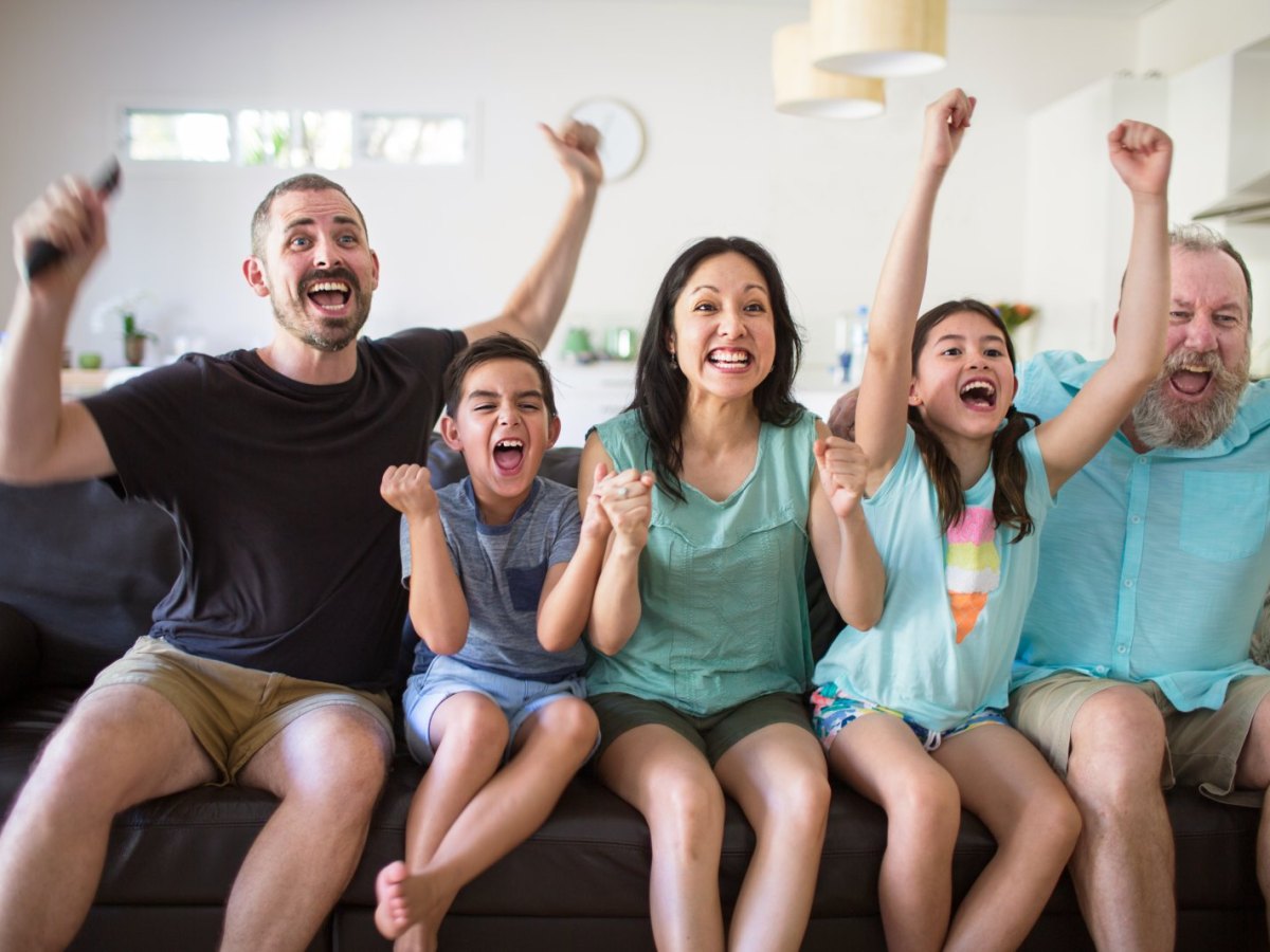 Familie sitzt auf dem Sofa und jubelt beim Fernsehen.