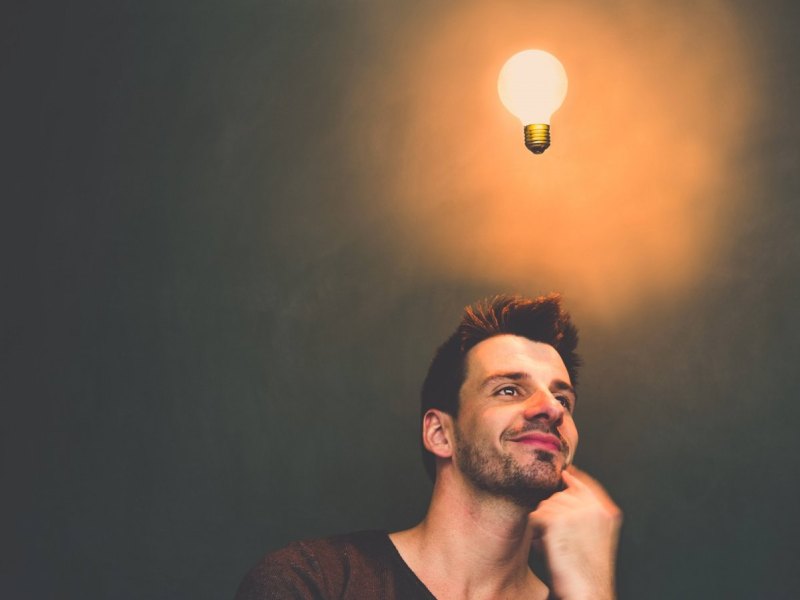 Nachdenkender Mann mit einer leuchtenden Glühlampe über dem Kopf