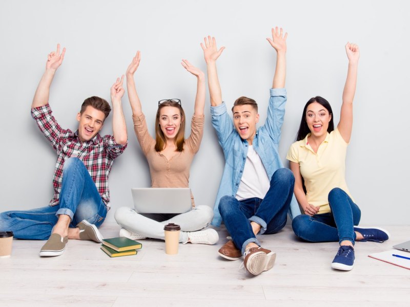 Vier Studenten arbeiten an ihren Laptops und freuen sich.