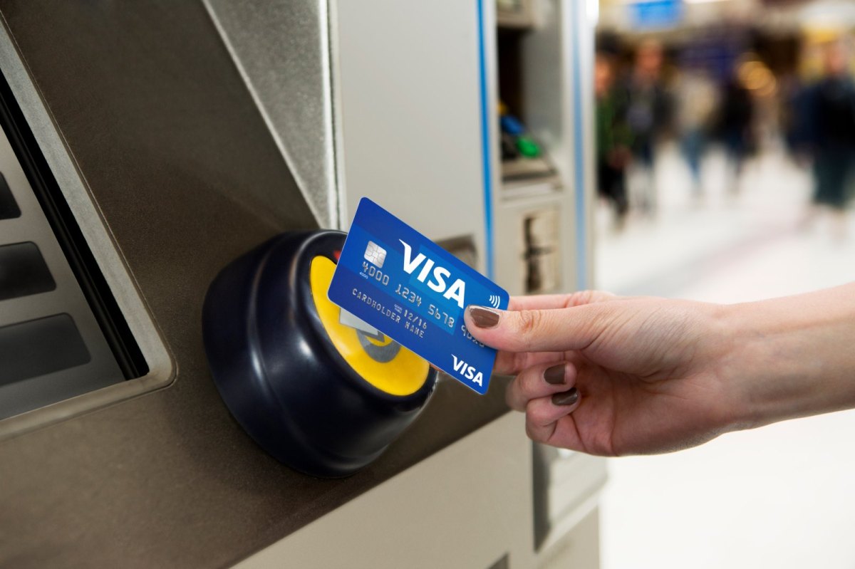 Frau bezahlt mit Visa Karte an einem Ticketautomaten.