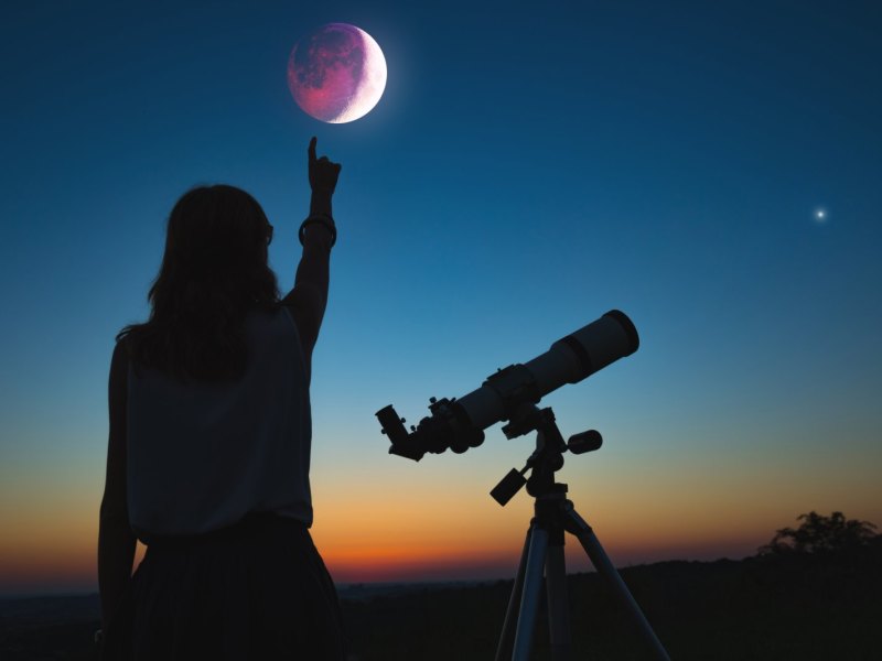 Frau mit Teleskop zeigt auf den Mond.