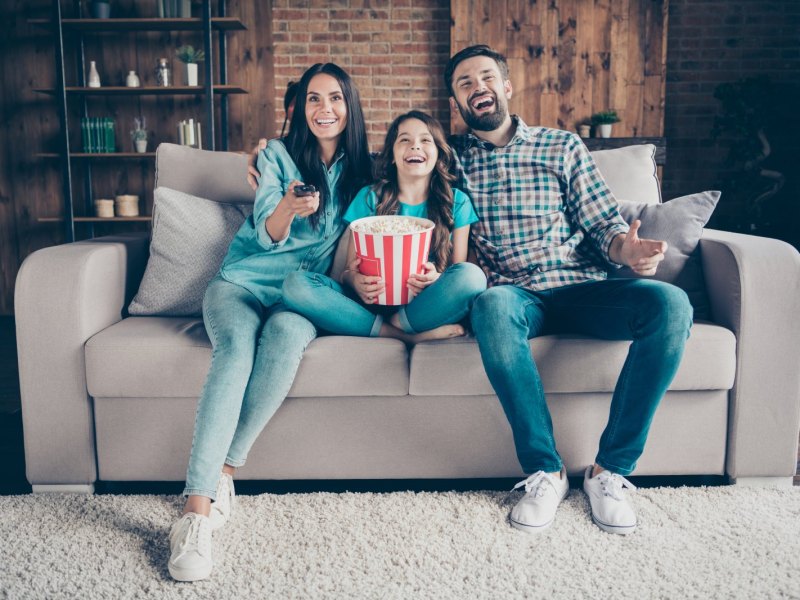 Eine Familie sitzt auf dem Sofa und sieht fröhlich fern.