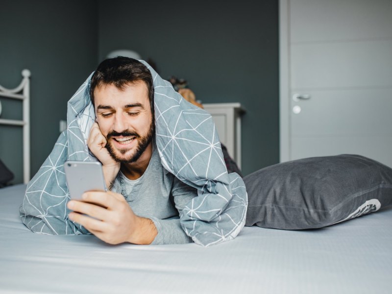 Mann blickt unter der Decke auf sein Handy.