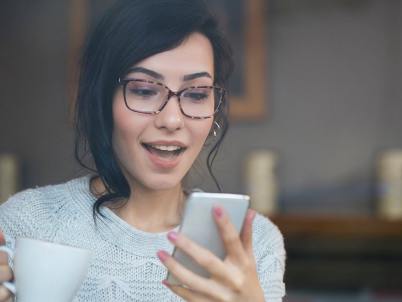 Frau blickt überrascht auf ihr Handy.