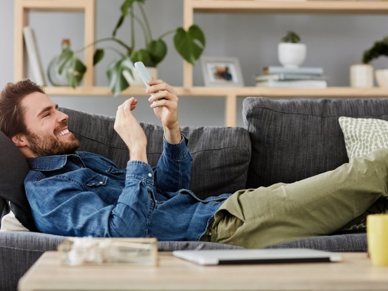 Mann liegt auf dem Sofa und beschäftigt sich mit seinem Handy.