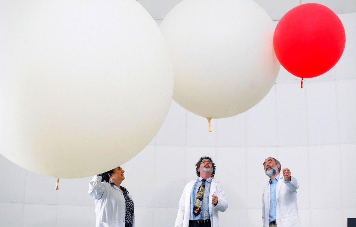 Menschen in Laborkitteln stehen unter drei Luftballons