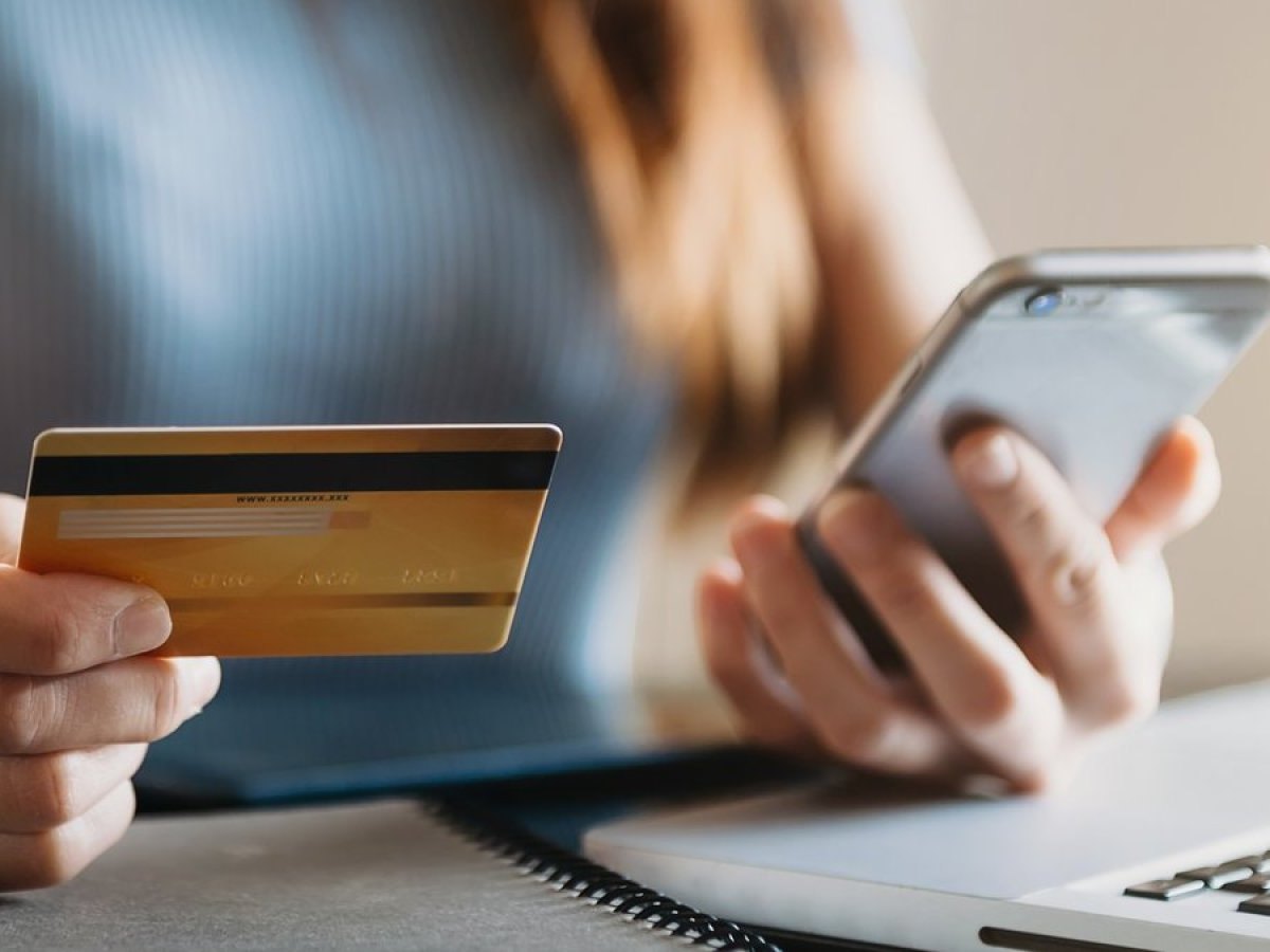 Frau hält ein Handy und eine Bankkarte in der Hand.