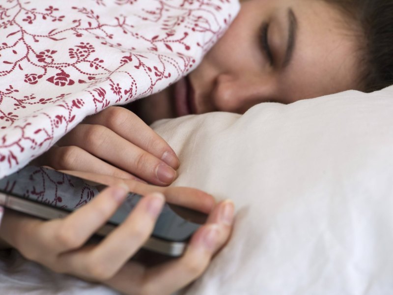 Frau im Bett mit Handy in der Hand