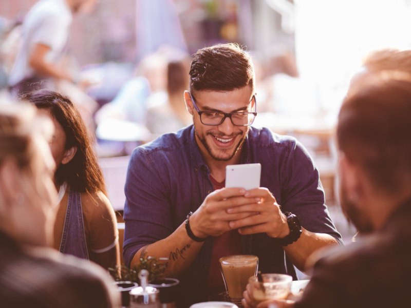 Mann sitzt im Café und schaut lachend auf sein Handy.