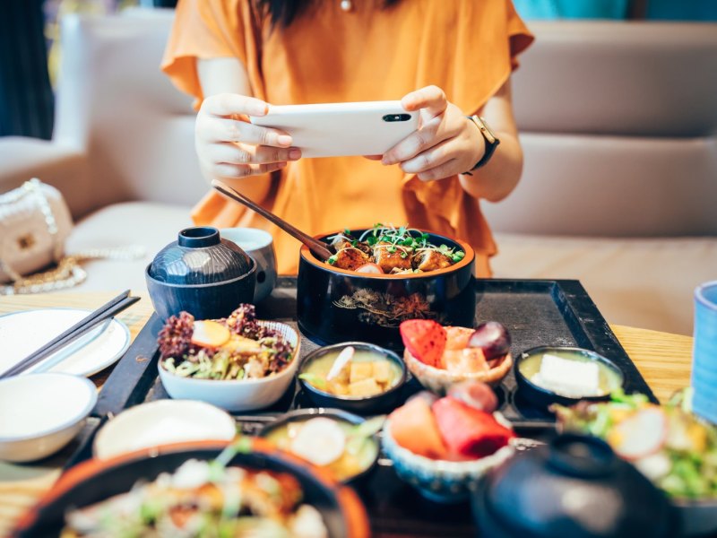 Frau macht ein Foto von asiatischem Essen.