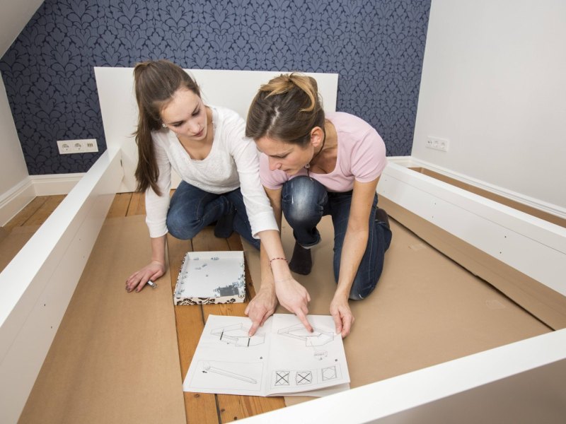 Frauen bauen ein Ikea-Bett zusammen.