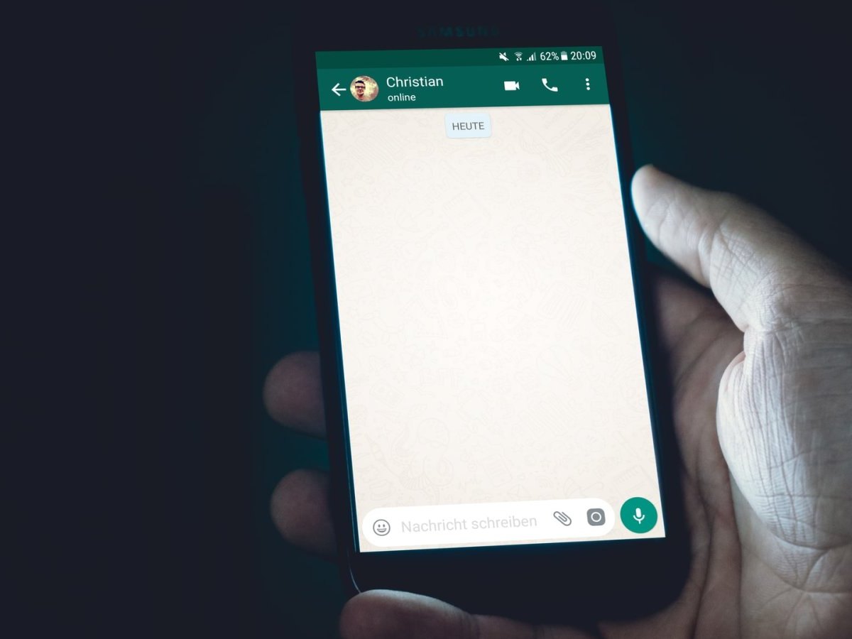 Ein Smartphone auf dem WhatsApp geöffnet ist in einer Hand.