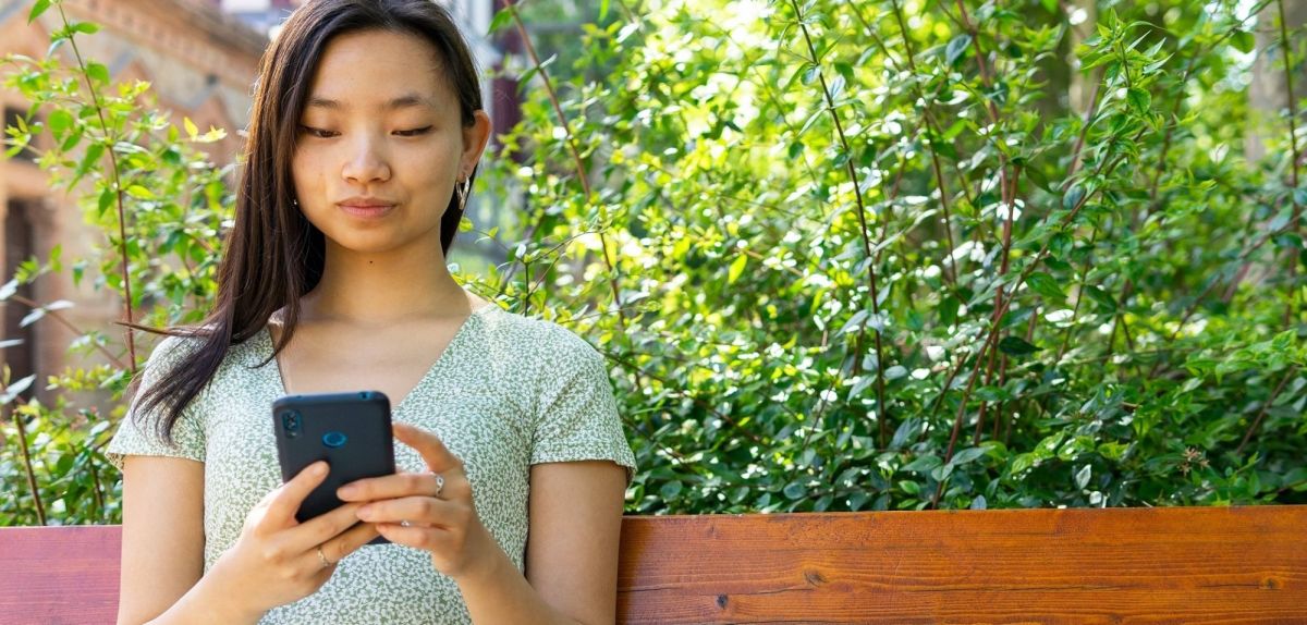 Frau sitzt mit Handy im Garten