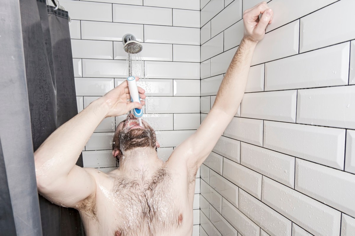 Mann unter der Dusche mit Zahnbürste