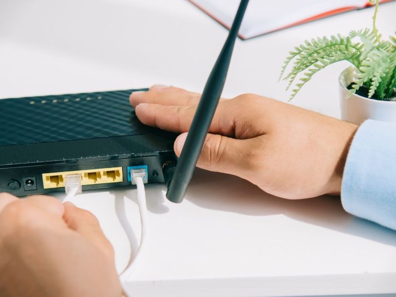 Person steckt Kabel in einen WLAN-Router