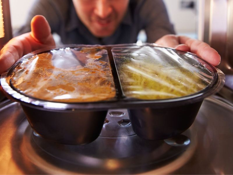 Mann schiebt Essen im Mini-Mikrowelle