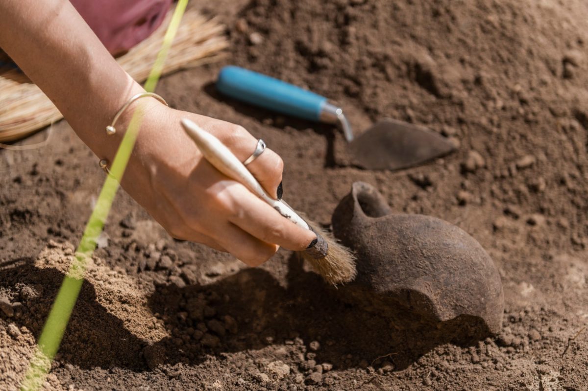 Eine Archäologin gräbt einen Keramikkrug mit Pinsel und Spachtel aus.