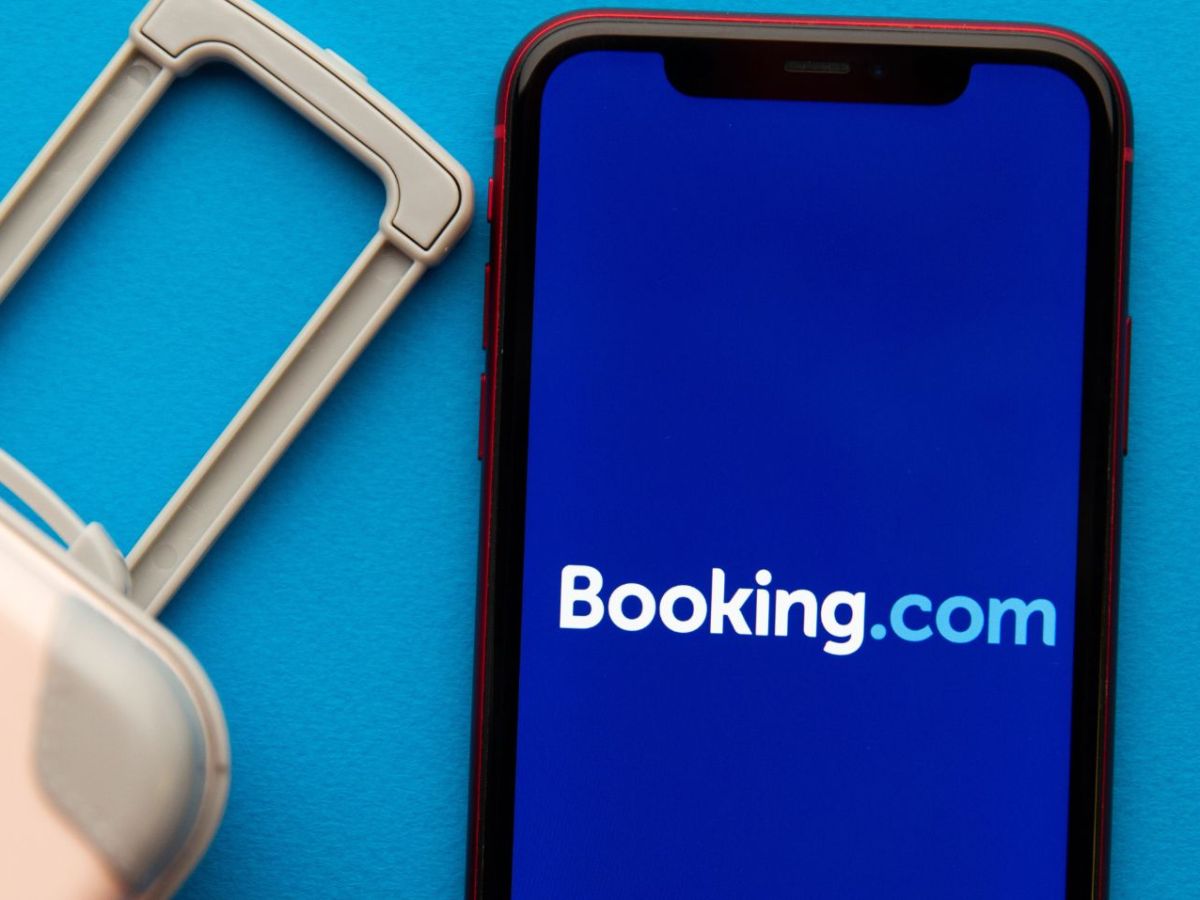 Booking.com-Schriftzug auf einem Handy, daneben ein Koffer.