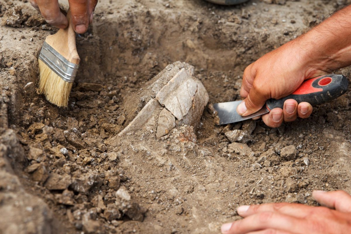 Hände graben mit Werkzeug an einem archäologischen Fund.