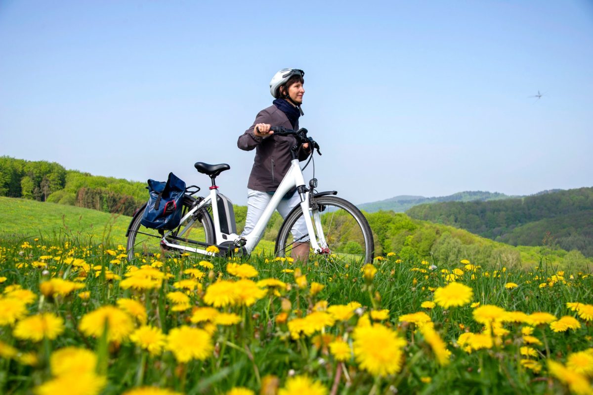 Frau geht mit einem Hollandrad als E-Bike durch eine Wiese.