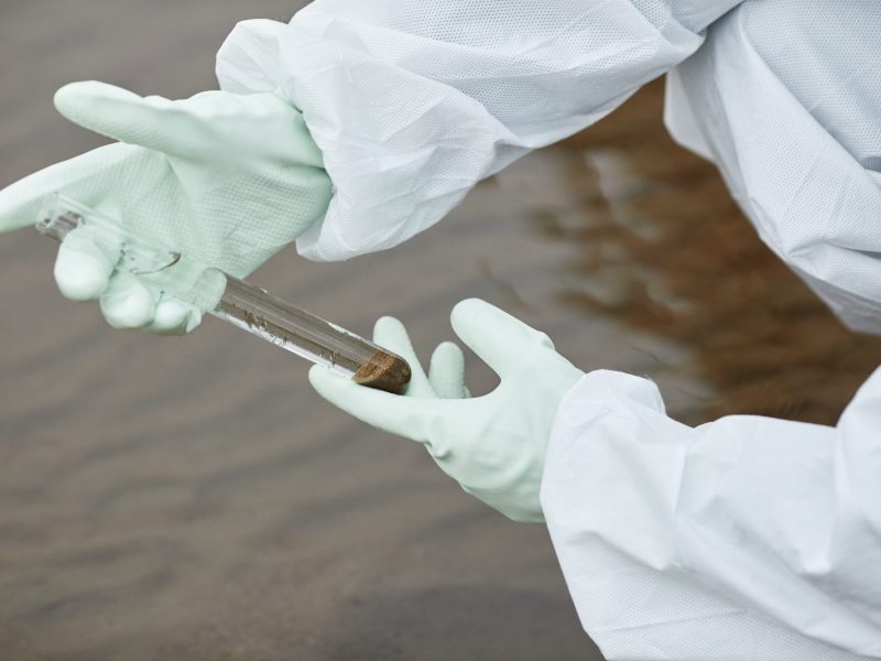Eine Person mit weißen Handschuhen hält eine Wasserprobe in der Hand.