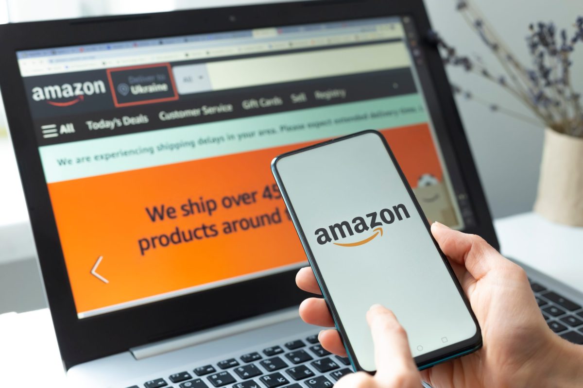 Amazon Logo auf einem Smartphone, im Hintergrund ist die Amazon-Website auf einem Laptop offen.