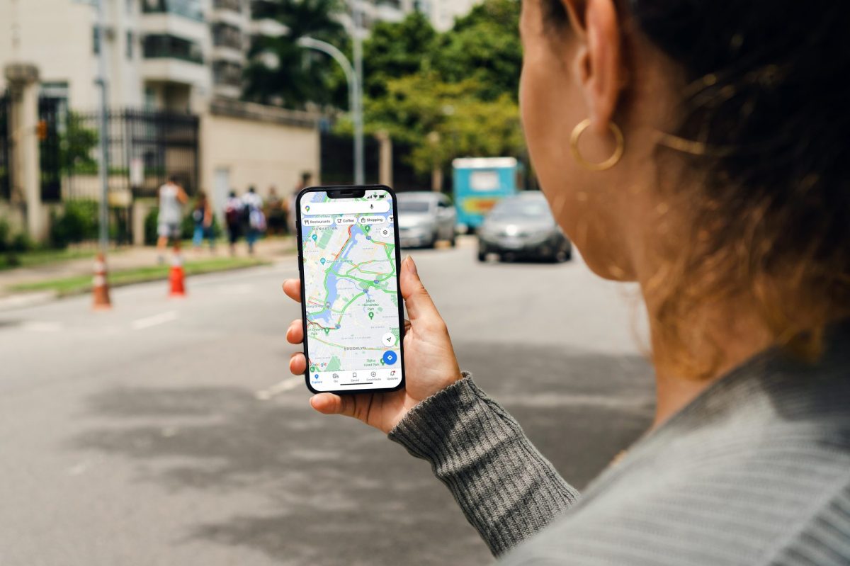 Eine Frau hält ein Handy in der Hand. auf dem Display ist die Kartenanzeige von Google Maps geöffnet. Dahinter ist eine Straße zu sehen.