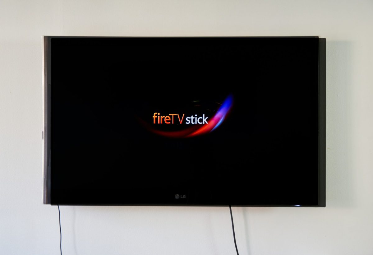 Ein Fernseher ist an der Wand befestigt, darauf ist das Logo des Amazon Fire TV Stick zu sehen.