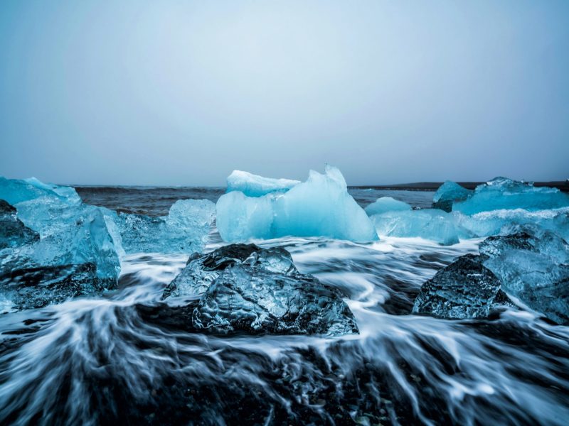 Eisformationen auf dunklem Stein vor einem weißen Himmel.