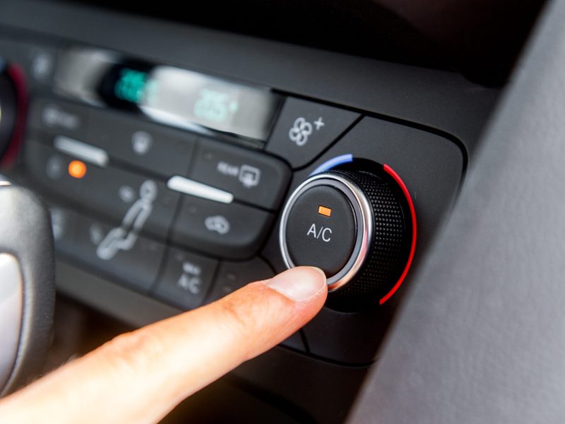 Hand tippt mit dem Finger auf die Schaltung der Klimaanlage im Auto.