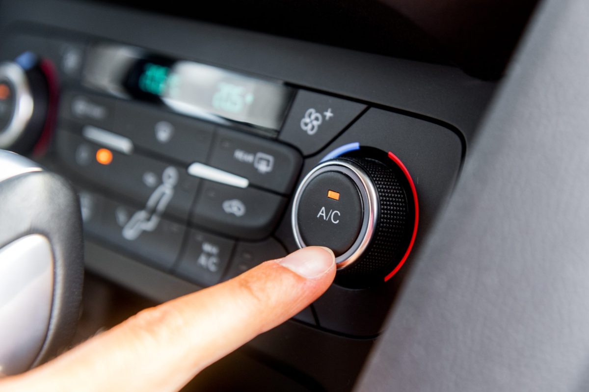 Hand tippt mit dem Finger auf die Schaltung der Klimaanlage im Auto.