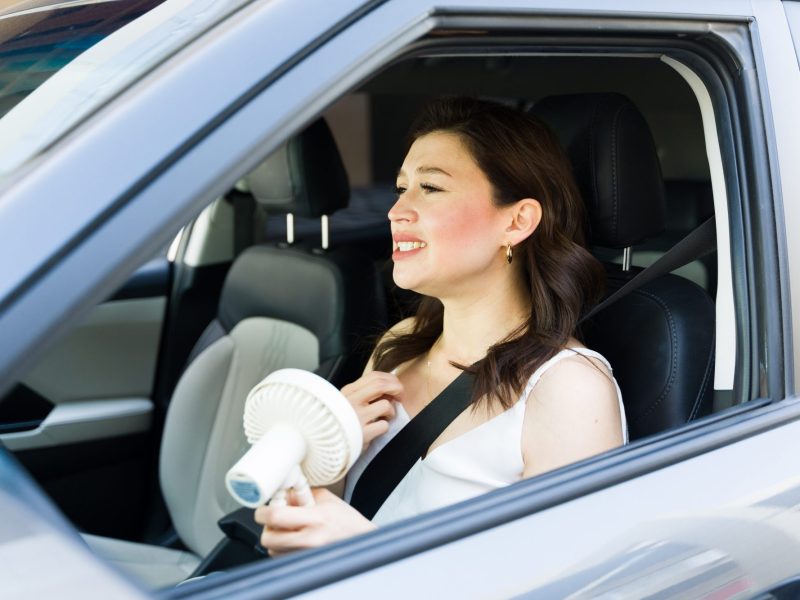 Frau in einem Auto nutzt einen Ventilator.
