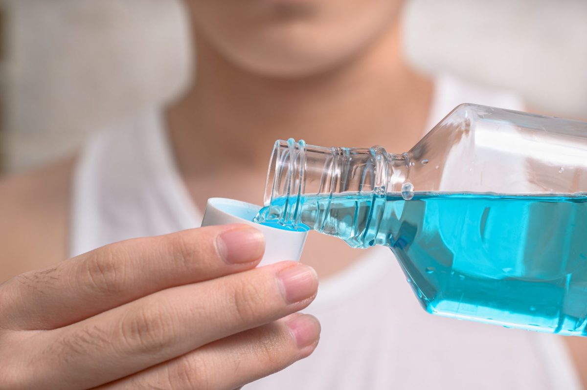 Eine Person gibt Mundwasser aus einer Flasche in eine Kappe.