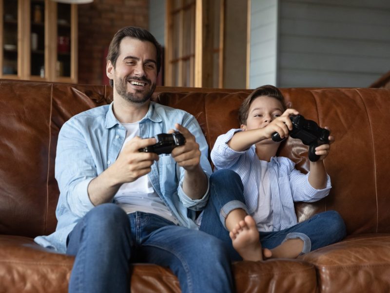 Ein Erwachsener und ein Kind spielen zusammen PlayStation.