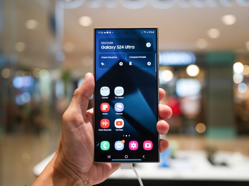 Eine Person hält ein Samsung Galaxy S24 in der Hand. Auf dem Display werden mehrere Widgets und Apps angezeigt.