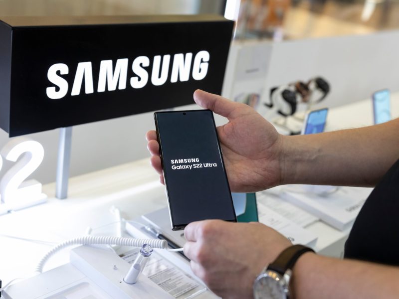Eine Person hält ein Samsung Galaxy-Gerät in den Händen. Im Hintergrund ist das Samsung-Logo zu sehen.