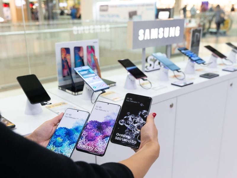 Person hält mehrere Samsung-Handys vor einer Auslage.