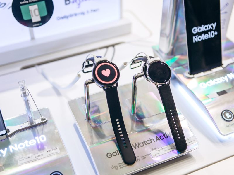 Zwei Samsung Galaxy Watches liegen neben einem Handy in einer Auslage.
