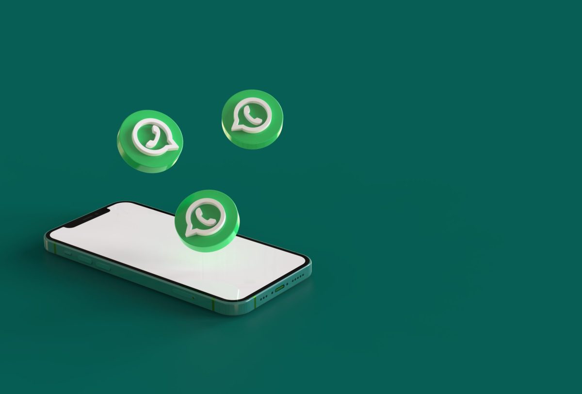 Ein Handy liegt auf einem grünen Untergrund. Darüber schweben drei WhatsApp-Logos.