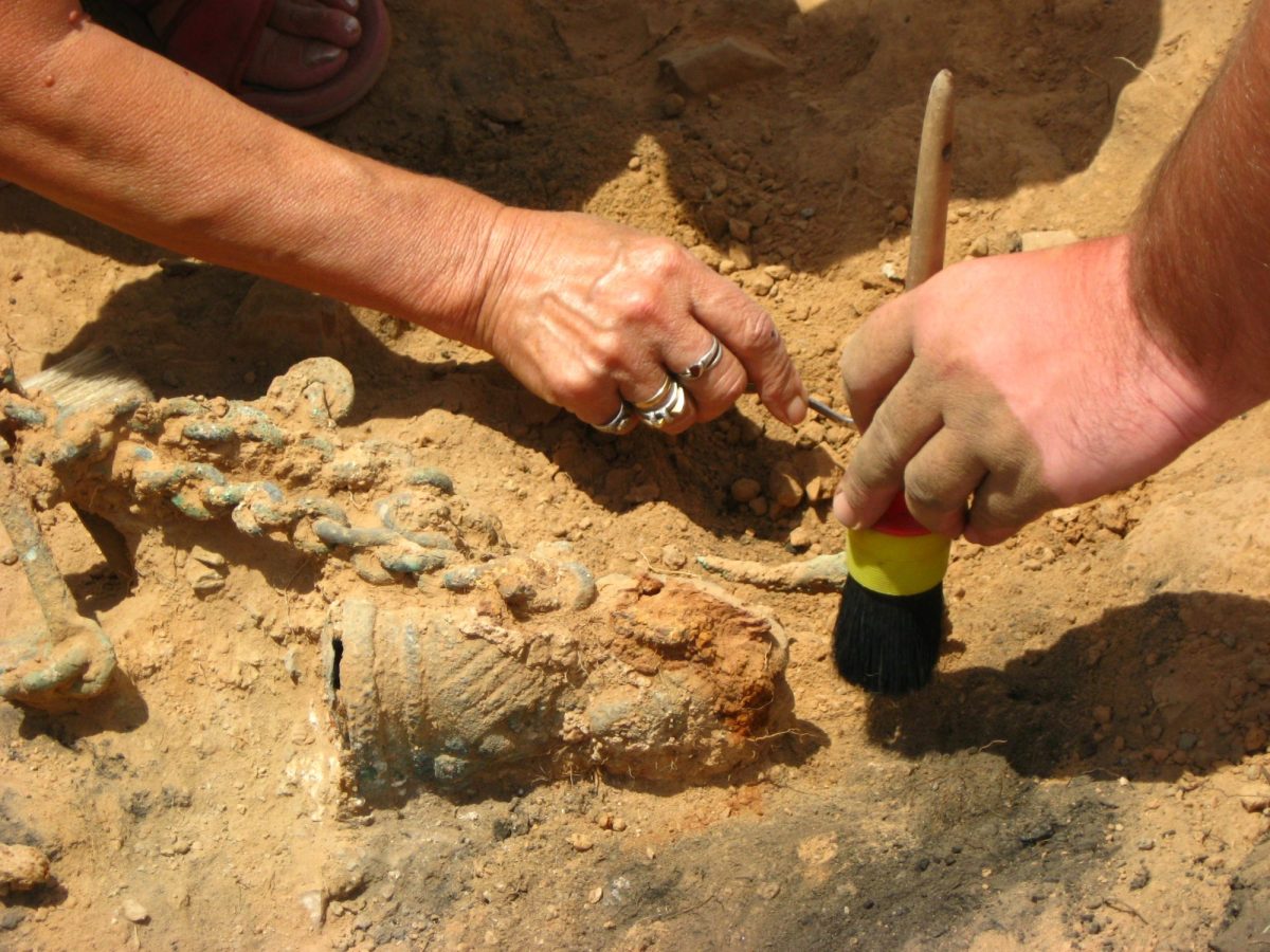 Hände arbeiten mit Werkzeug an einem archäologischen Fund.