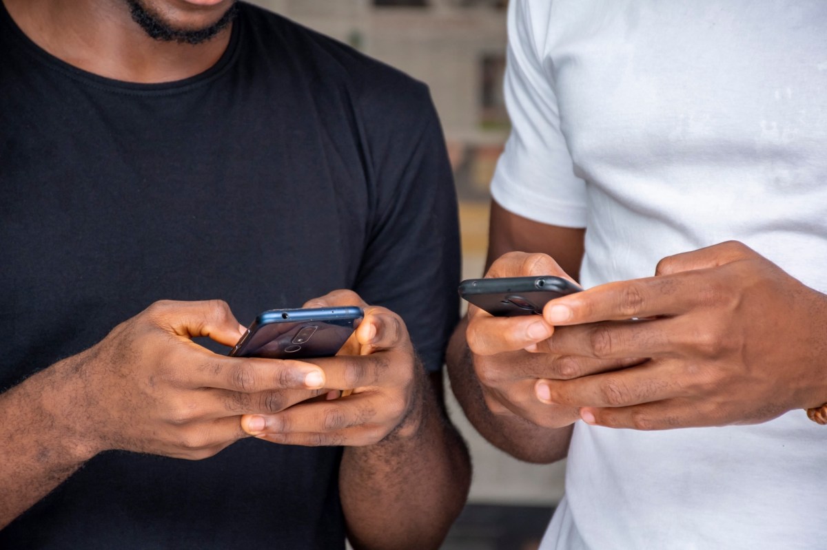 Zwei Menschen stehen nebeneinander und tippen auf den Bildschirmen ihrer Smartphones.