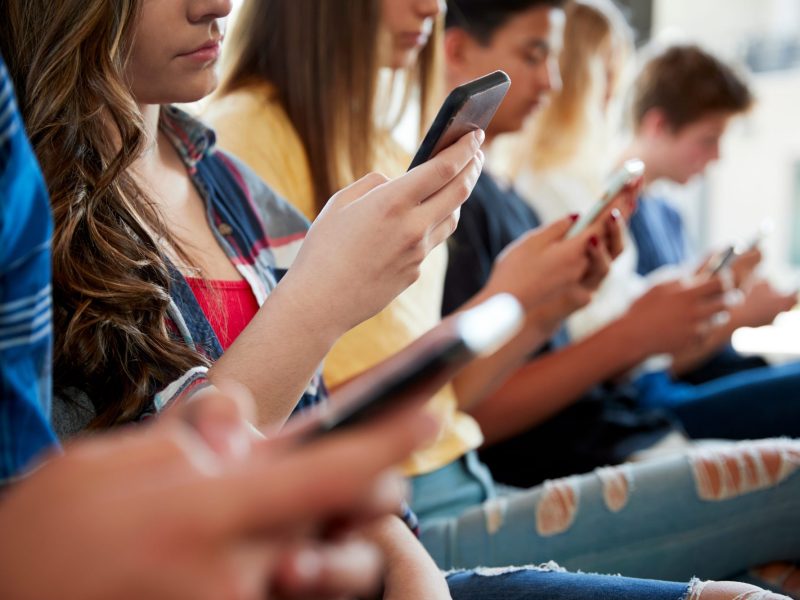 Jugendliche sitzen in einer Reihe nebeneinander und halten jeweils ein Smartphone in der Hand.