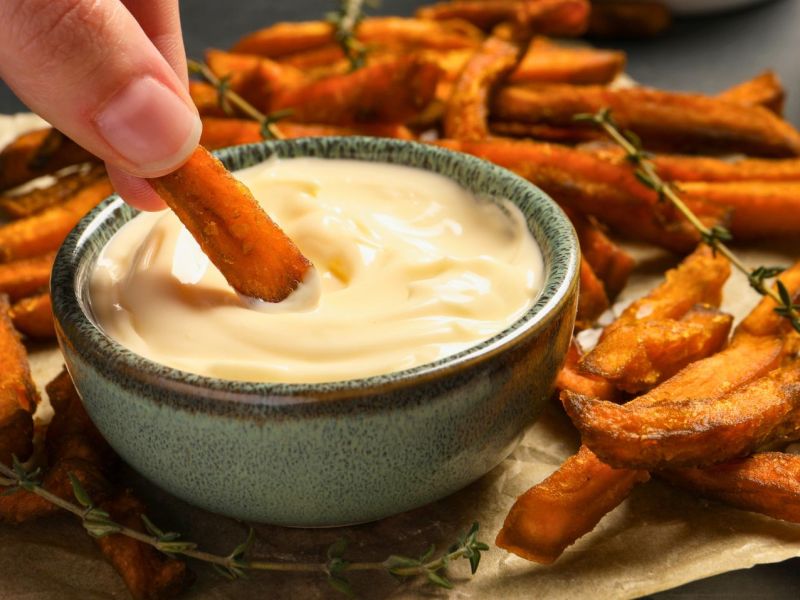 Süßkartoffel-Pommes werden in Mayonnaise getunkt.