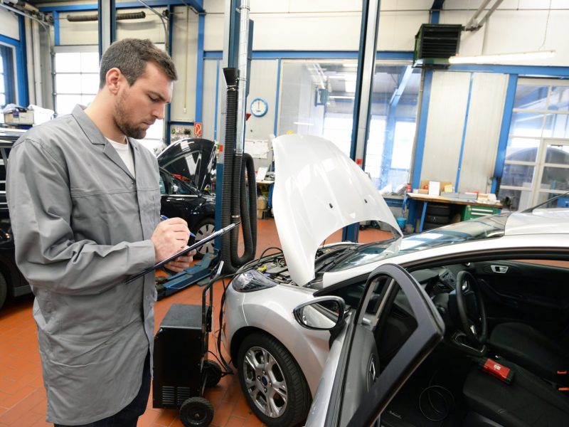 Prüfer vom TÜV mit einem Auto und Klemmbrett.