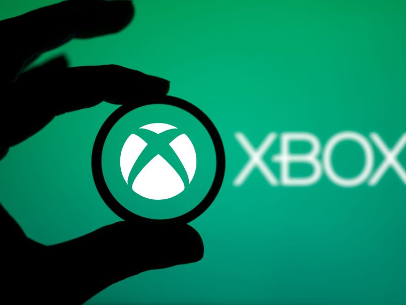 Das Xbox-Logo ist auf einem grünen Hintergrund zu sehen. Im Vordergrund ist der Schatten einer Hand zu sehen.