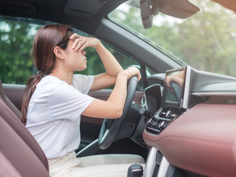 Frau sitzt am Steuer eines Autos und hält sich verzweifelt die Hand vor das Gesicht.