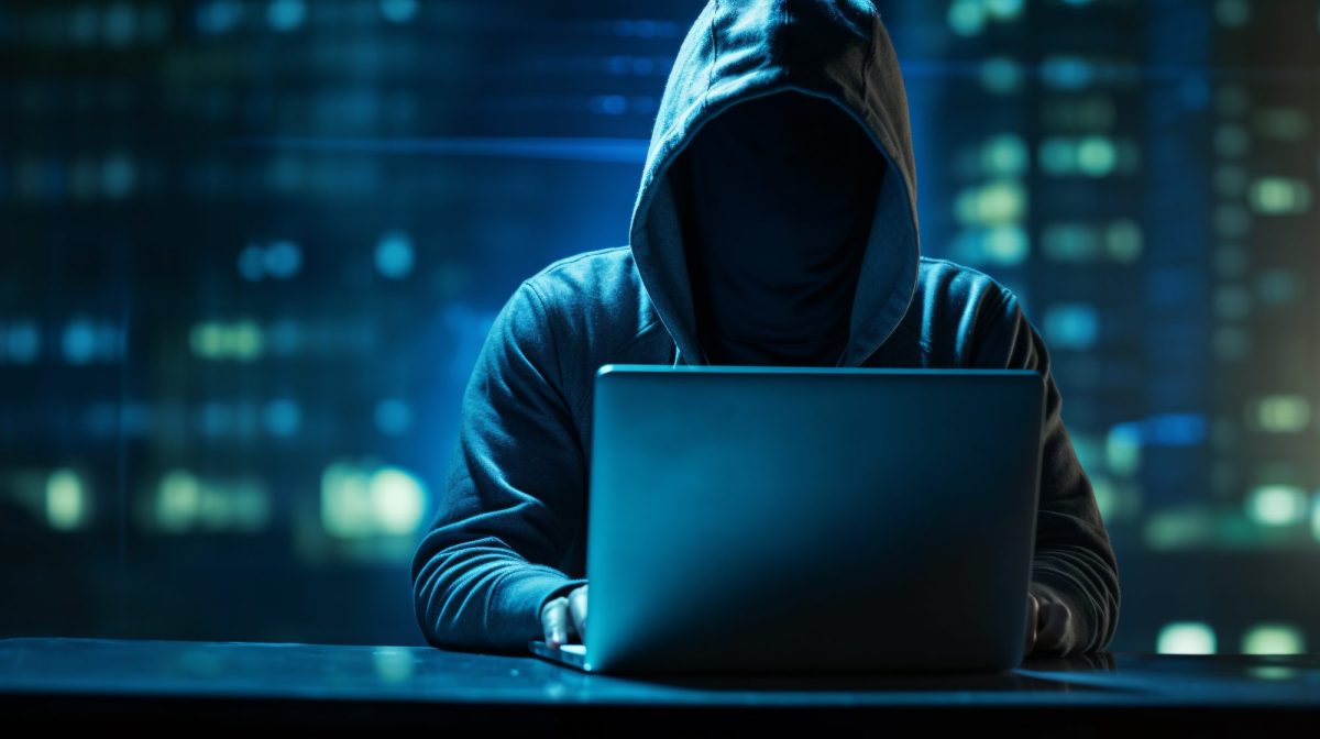 Hacker sitzt mit aufgezogener Kapuze vor einem Laptop.