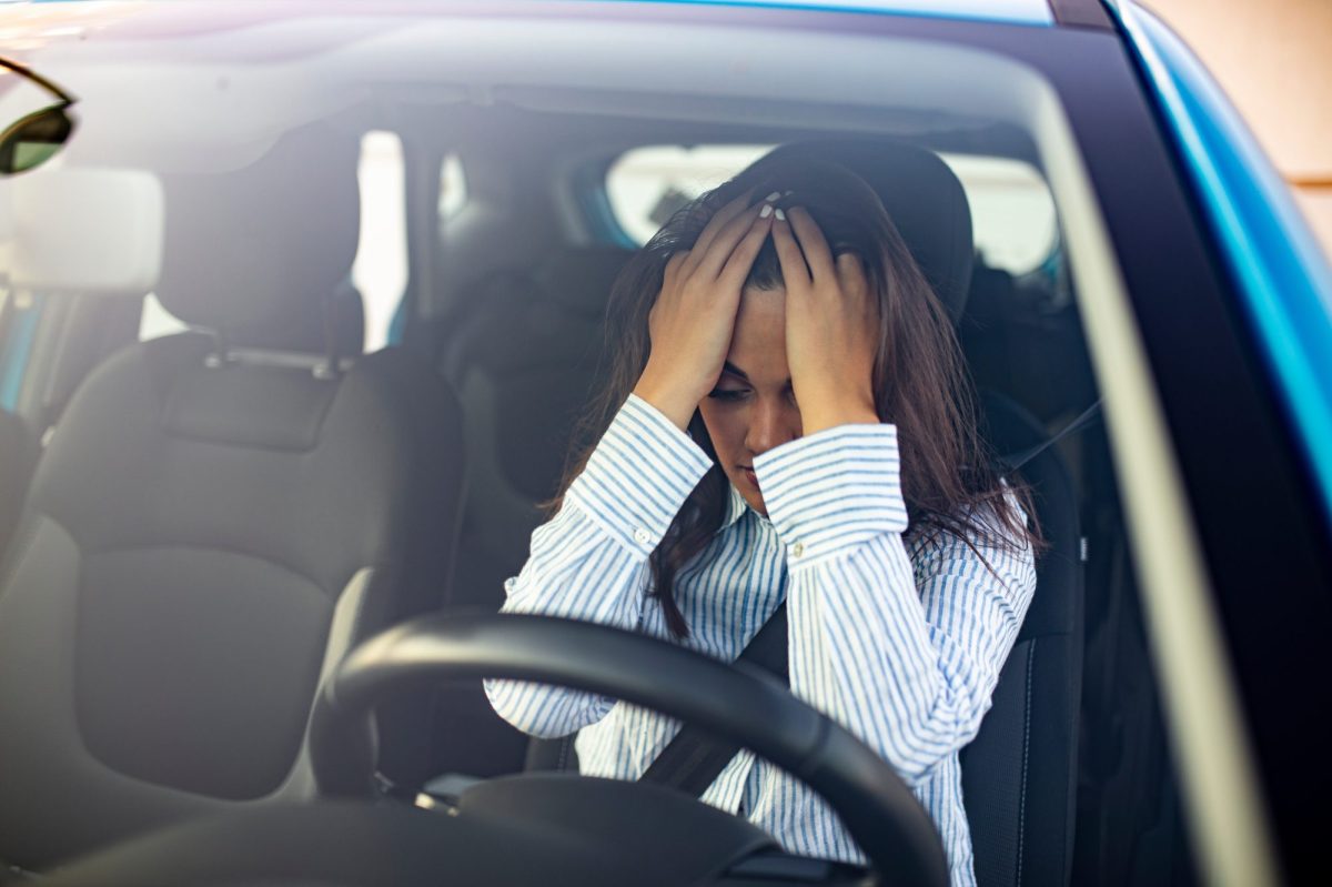 Verzweifelte Person hält sich im Auto die Hände vors Gesicht.